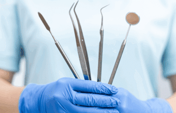 Dentist holding sterilized instruments including mirror, explorer, and tweezers for dental examination.