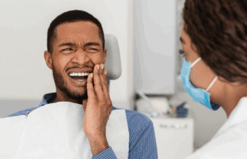 Patient experiencing tooth pain during emergency dental consultation with dentist.
