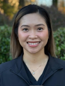 Young woman smiling at camera wearing black shirt, outdoor blurred green background