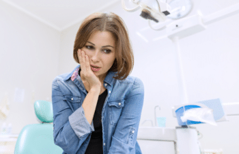 Woman holding her cheek in discomfort at a dental office, illustrating signs of a dental emergency.