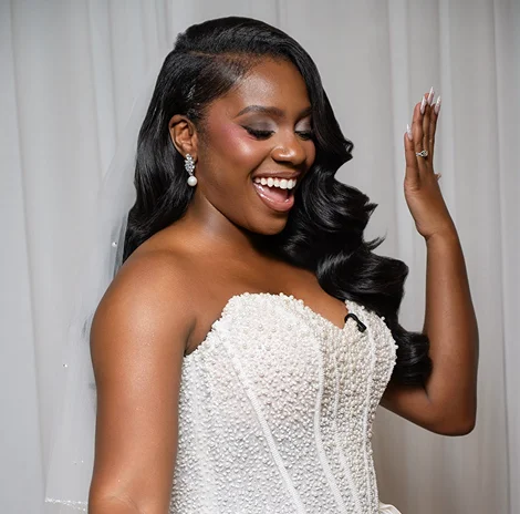 Woman in a white embellished wedding dress smiling with her hand raised.