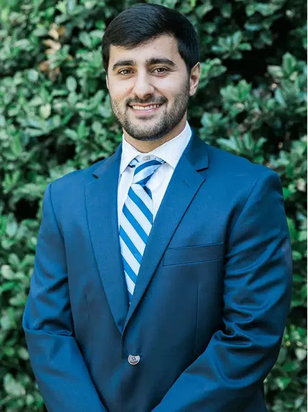 Dr. Kasra Nezafat wearing a blue suit and striped tie, smiling outdoors.